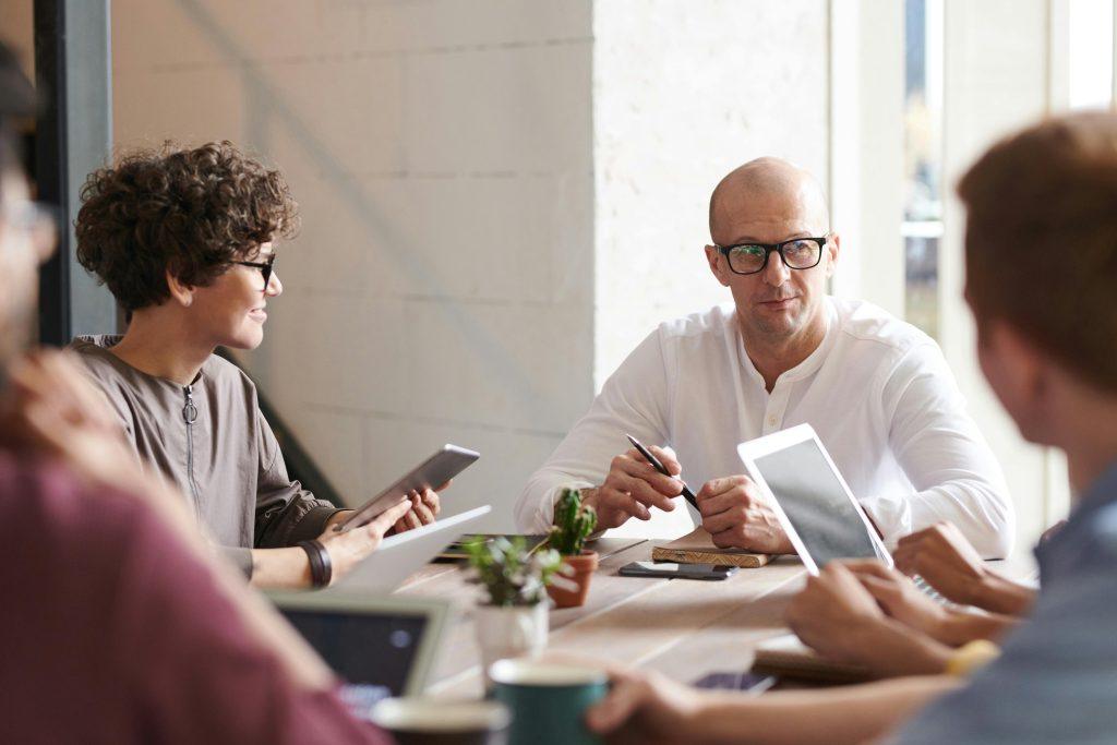 Personas en una oficina sentados en una mesa, trabajando y hablando.